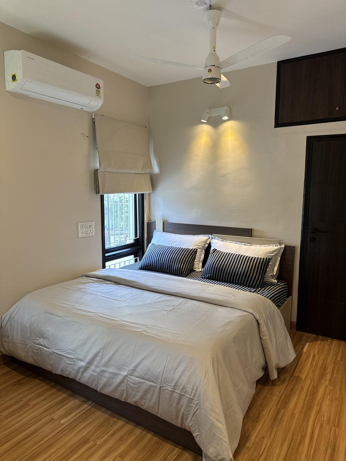 A king bed with grey linen and striped cushions under two wall lights